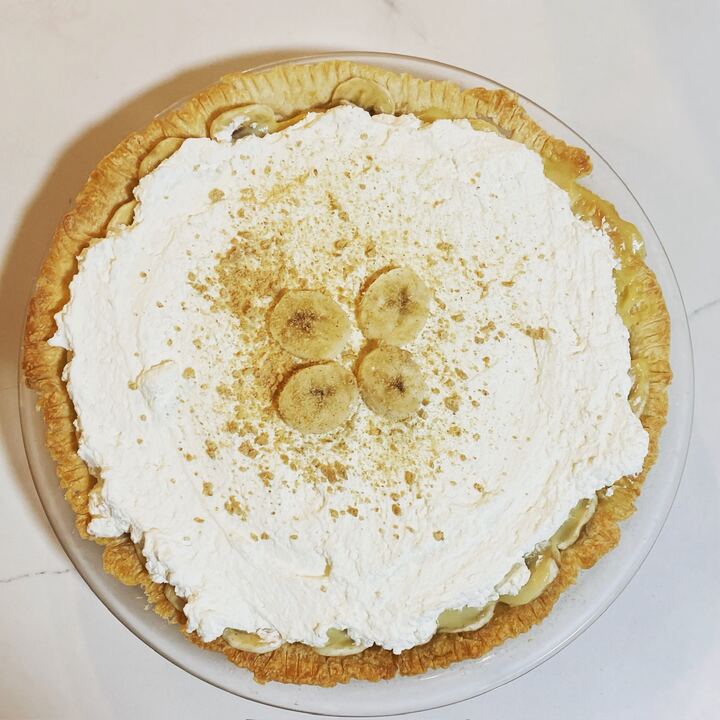 Banana cream pie topped with whipped cream, banana slices and crumbs