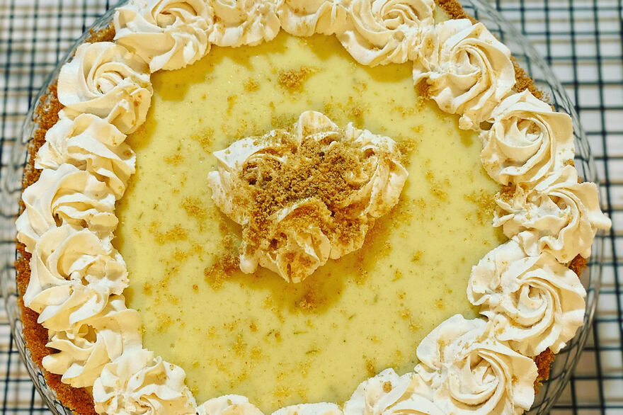 Key lime pie on a graham cracker crust, edged with piped whipped cream rosettes and dusted with graham crumbs