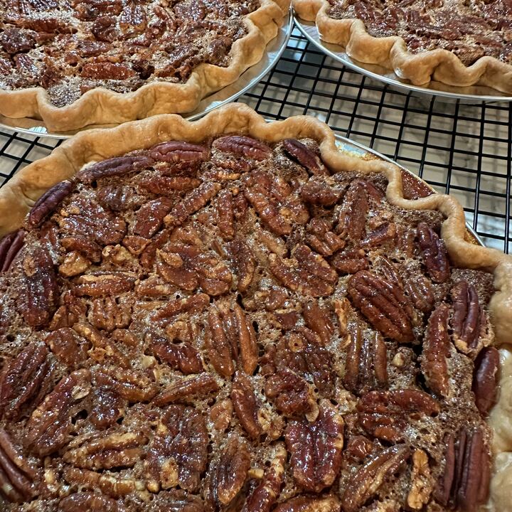 Three pecan pies cooling on a wire rack, packed with toasted pecan halves